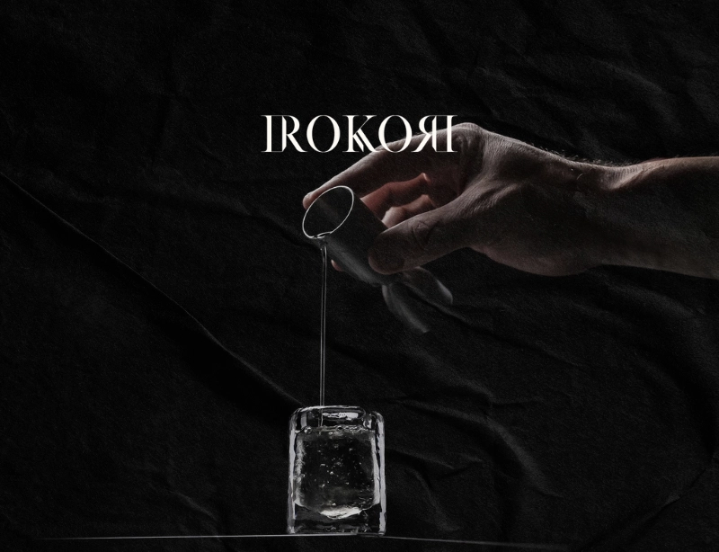Mano vertiendo una bebida en un vaso de hielo cristalino de Irokori sobre fondo negro, diseño web de KLOROFiLA